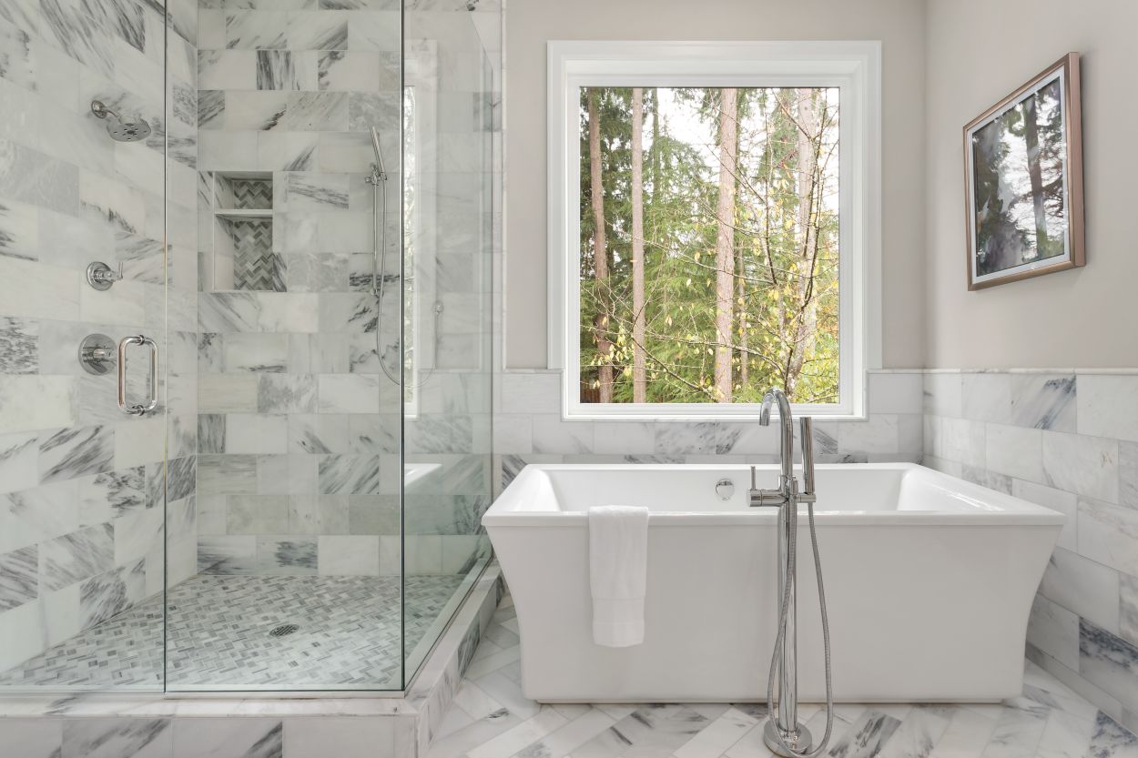 Bathroom with bathtub and shower in new luxury home with all glass shower. Large window allows for abundant natural light.