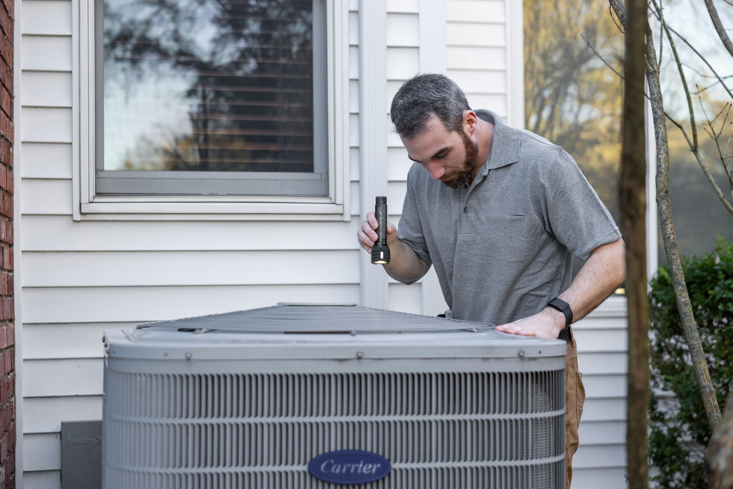 a technician inspecting the outdoor condenser unit of a home AC system. - ac service in escondido